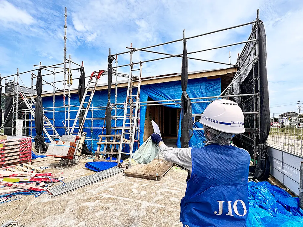 構造躯体検査に立ち会うJIO検査員と足場に囲まれた「ゆとりの庭で趣味を愉しむ平屋」の外観