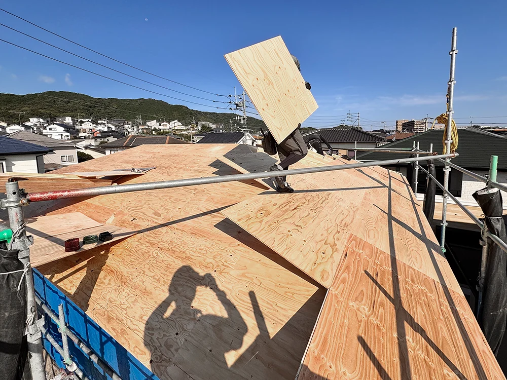 屋根下地の合板を運ぶ職人