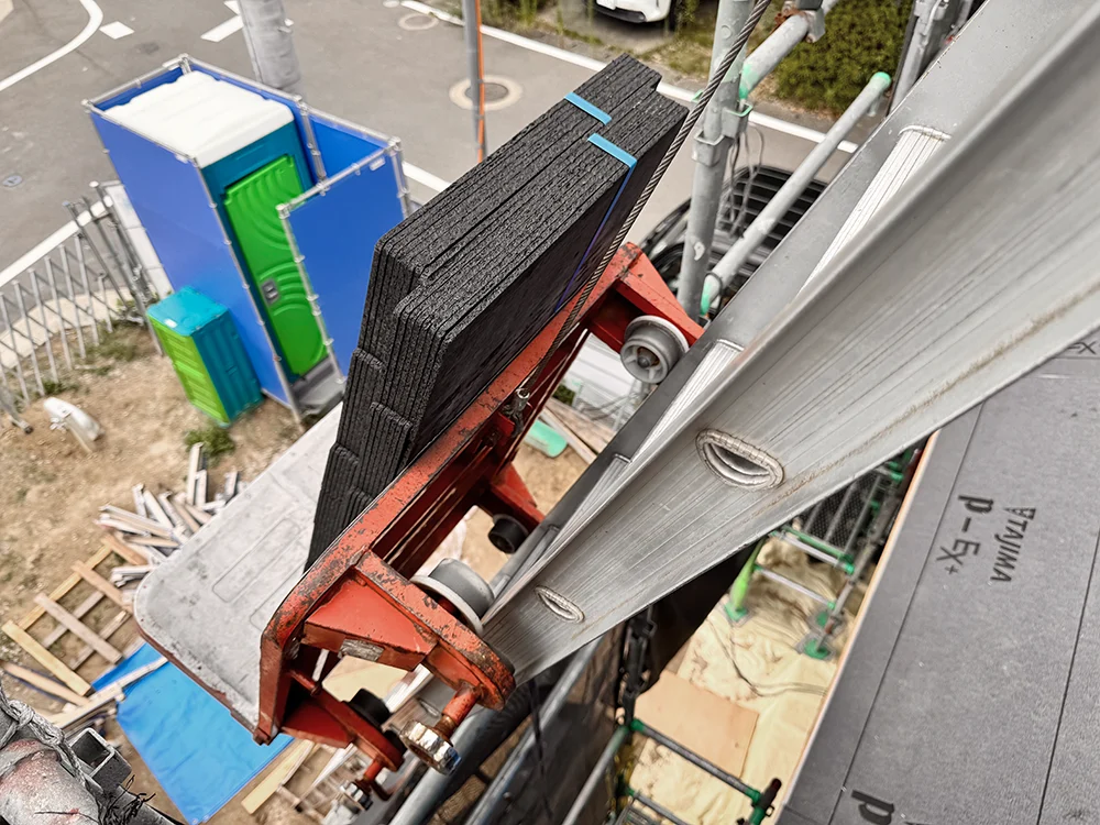 荷揚げ機で屋根の上へ運ばれるスレート瓦