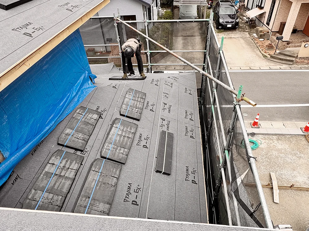 屋根の上でスレート瓦の取り付け準備を進める職人
